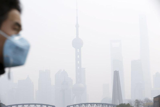 A man wearing a face mask walks on a bridge in front of the financial district of Pudong amid heavy smog in Shanghai, China, December 15, 2015. REUTERS/Aly Song